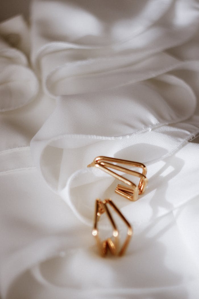 Stylish gold earrings elegantly placed on delicate white fabric, creating a luxurious and soft feel.